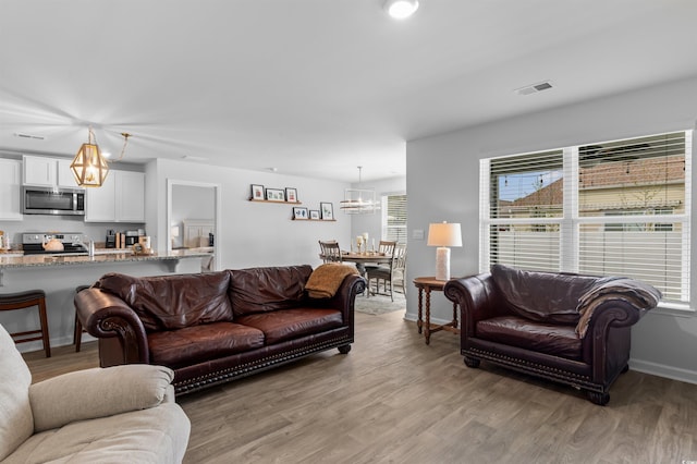 living area with an inviting chandelier, light wood-style floors, baseboards, and visible vents