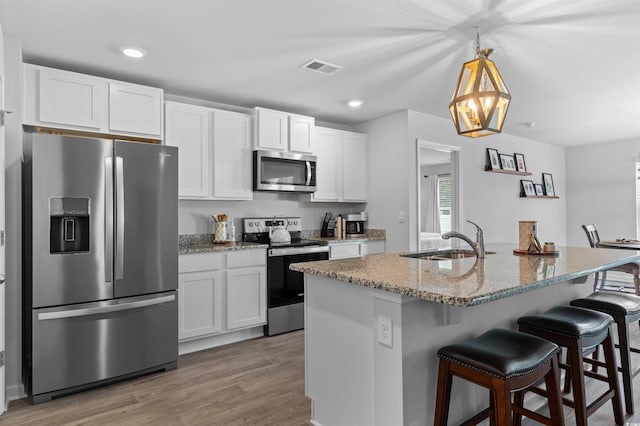 kitchen featuring light stone countertops, a sink, white cabinets, a breakfast bar, and stainless steel appliances