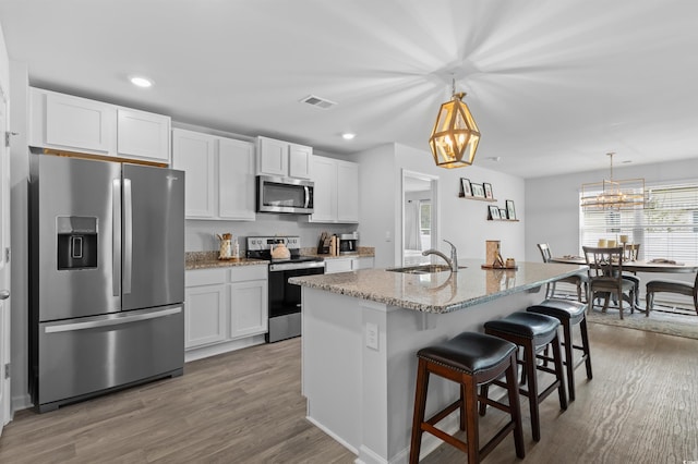 kitchen featuring appliances with stainless steel finishes, a sink, wood finished floors, visible vents, and a center island with sink