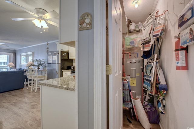 hallway with water heater, ornamental molding, and light wood-style floors