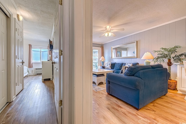 living area with light wood finished floors, a textured ceiling, a ceiling fan, and ornamental molding
