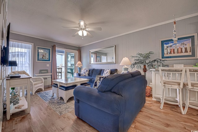 living area with a textured ceiling, light wood-type flooring, crown molding, and ceiling fan