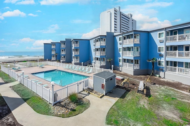 pool with a patio, an outbuilding, a water view, fence, and a storage unit