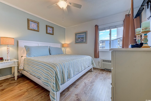 bedroom with baseboards, a ceiling fan, a wall mounted AC, crown molding, and wood finished floors