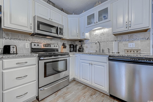kitchen with stainless steel appliances, white cabinets, a sink, and light wood-style flooring