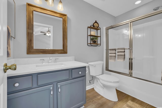 bathroom with combined bath / shower with glass door, baseboards, toilet, wood finished floors, and vanity