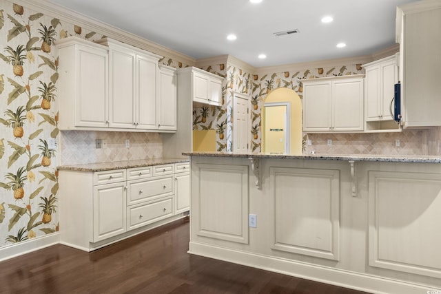 kitchen featuring visible vents, dark wood-style flooring, wallpapered walls, and light stone counters