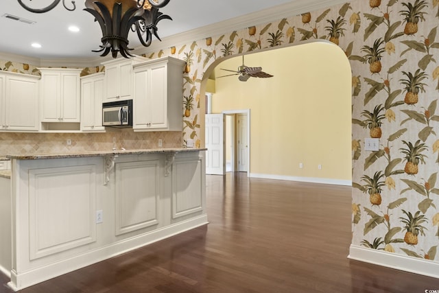 808 E Coast Ln, North Myrtle Beach, SC 29582 - kitchen featuring arched walkways, stainless steel microwave, wallpapered walls, light stone counters, and ornamental molding