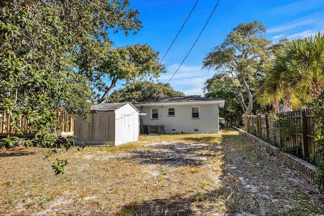 back of house featuring crawl space, a storage shed, central AC, an outdoor structure, and a fenced backyard