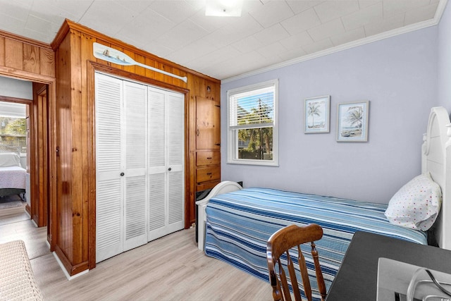 bedroom with crown molding, wood walls, a closet, and light wood finished floors