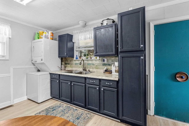 kitchen featuring visible vents, stacked washer / drying machine, a sink, light wood finished floors, and ornamental molding