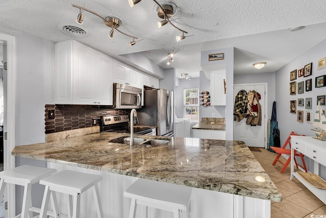 157 Egret Run Ln Unit 514, Pawleys Island, SC 29585 - kitchen featuring appliances with stainless steel finishes, a peninsula, decorative backsplash, light stone countertops, and a textured ceiling