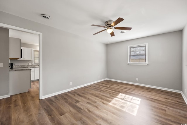 empty room with baseboards, wood finished floors, and ceiling fan