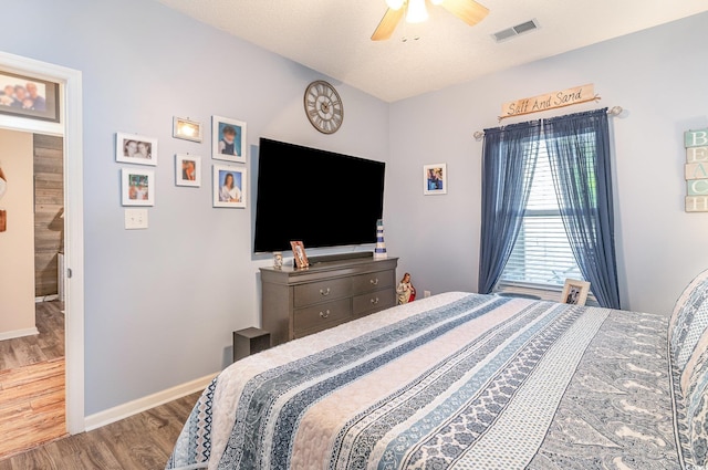 bedroom with ceiling fan, visible vents, baseboards, and wood finished floors