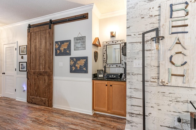 interior space with a barn door, a textured ceiling, crown molding, and wood finished floors