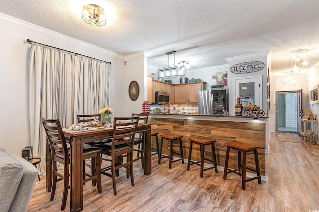 dining area featuring light wood finished floors, a textured ceiling, an inviting chandelier, and ornamental molding