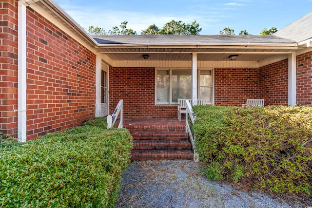 doorway to property with brick siding and covered porch