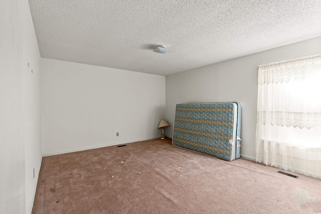 empty room with carpet flooring, a textured ceiling, and visible vents