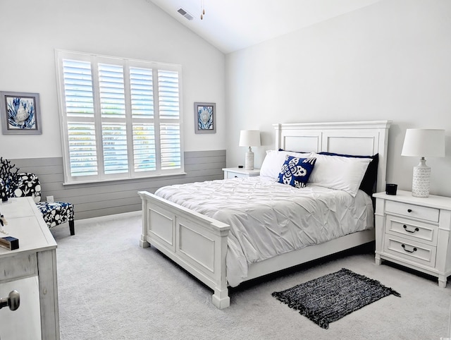 bedroom featuring light carpet, vaulted ceiling, and wainscoting