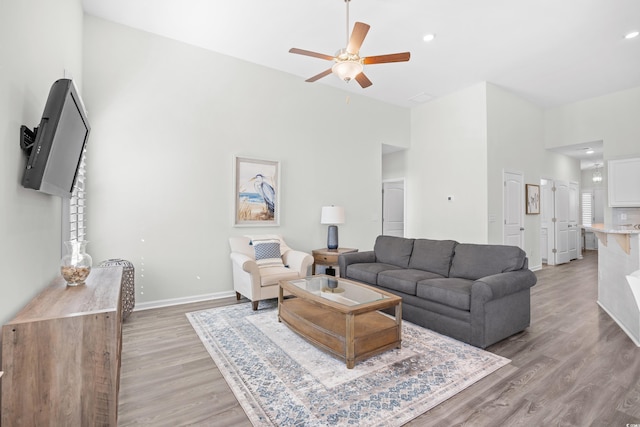 living area featuring light wood-style flooring, ceiling fan, baseboards, a high ceiling, and recessed lighting