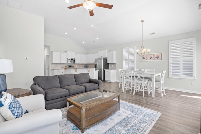 living room featuring a ceiling fan, vaulted ceiling, a chandelier, light wood-type flooring, and recessed lighting