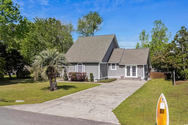 cape cod-style house with a front yard, french doors, roof with shingles, and concrete driveway