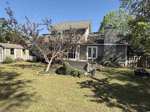 rear view of house with a chimney, french doors, fence, and a yard