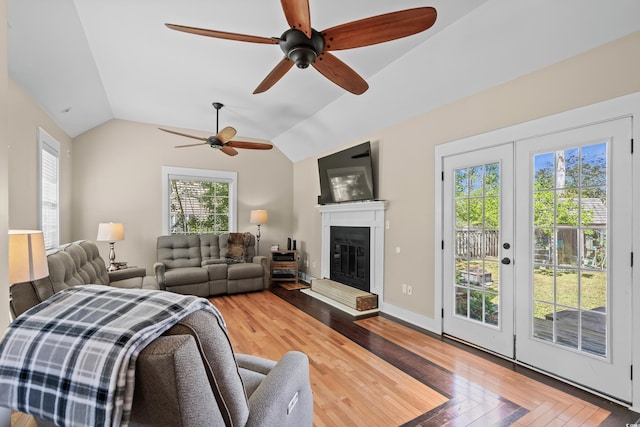 living room featuring a glass covered fireplace, wood finished floors, vaulted ceiling, and ceiling fan