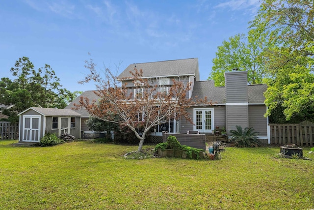 back of property with an outbuilding, a lawn, a storage unit, fence, and french doors