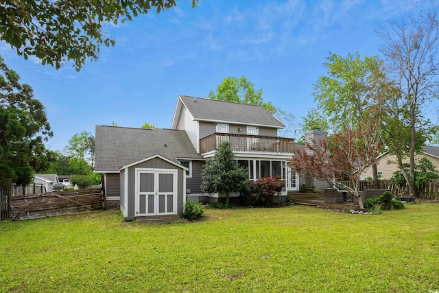 back of house with an outbuilding, a storage shed, a lawn, fence, and a shingled roof