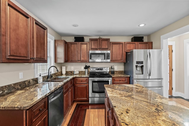 kitchen featuring a sink, recessed lighting, wood finished floors, stainless steel appliances, and stone counters