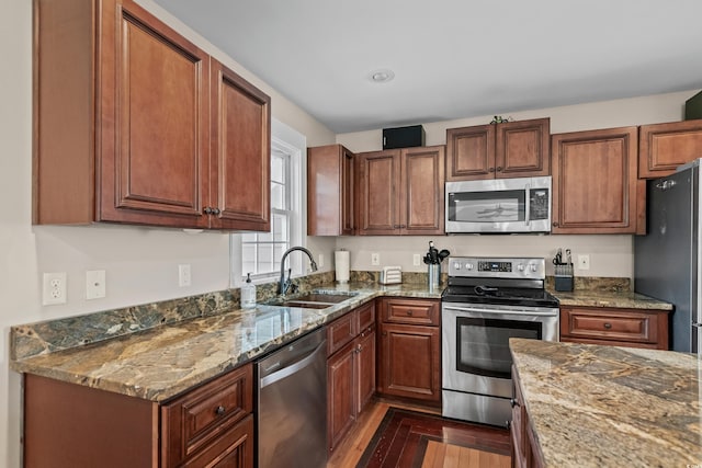 kitchen with stone counters, dark wood-type flooring, a sink, and appliances with stainless steel finishes