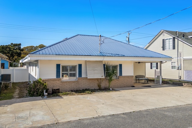 bungalow-style house featuring central air condition unit, metal roof, fence, and brick siding