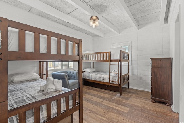 bedroom featuring multiple windows, beamed ceiling, and wood finished floors