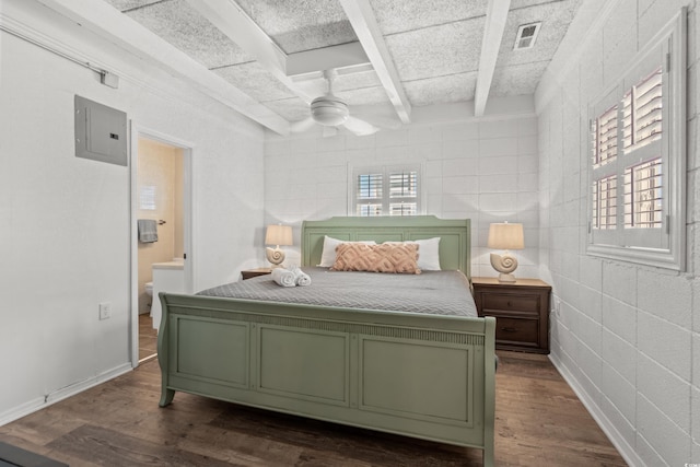 bedroom featuring electric panel, beamed ceiling, connected bathroom, and dark wood finished floors