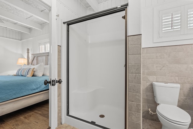 ensuite bathroom with toilet, connected bathroom, a stall shower, and wood finished floors