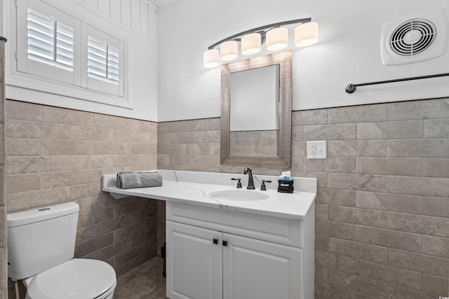 half bath with vanity, toilet, visible vents, wainscoting, and tile walls