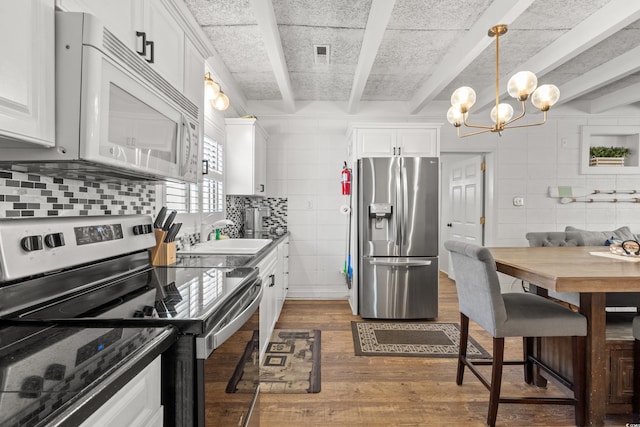kitchen with a sink, tile walls, appliances with stainless steel finishes, and dark wood-type flooring