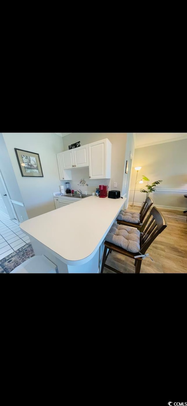 4669 Wild Iris Dr Unit 22-2O2, Myrtle Beach, SC 29577 - kitchen featuring a breakfast bar area, white cabinetry, light countertops, wood finished floors, and a peninsula