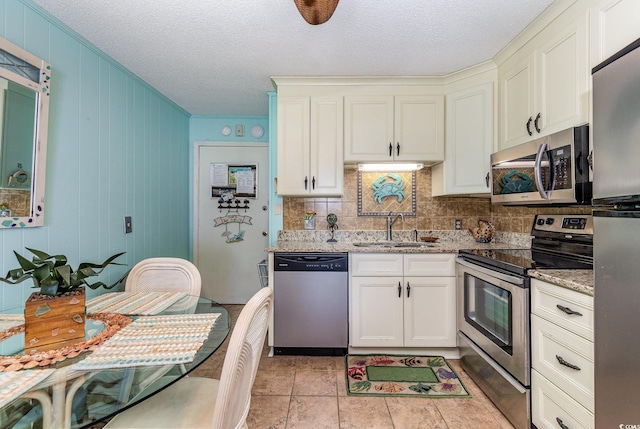 kitchen with appliances with stainless steel finishes, a sink, decorative backsplash, light stone countertops, and a textured ceiling