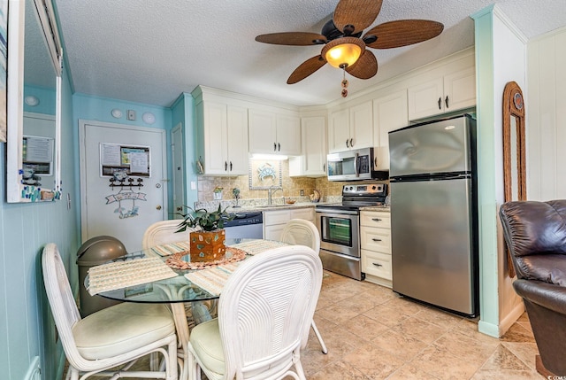 kitchen with appliances with stainless steel finishes, a sink, ceiling fan, light countertops, and white cabinetry