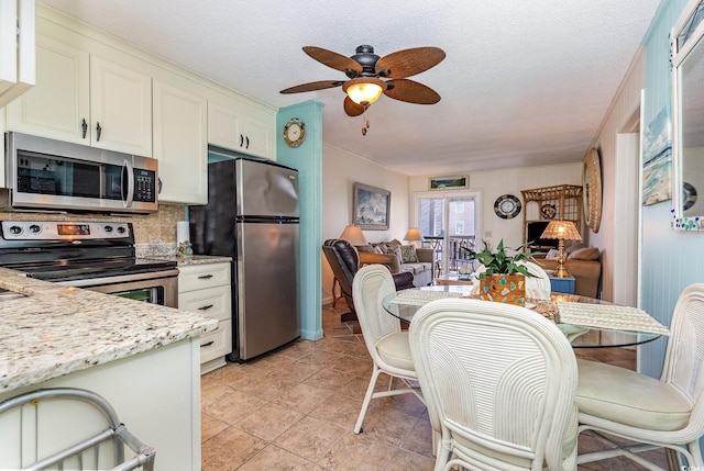 kitchen with stainless steel appliances, a ceiling fan, decorative backsplash, white cabinets, and open floor plan