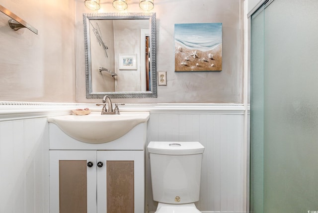 bathroom featuring wainscoting, toilet, vanity, and a decorative wall