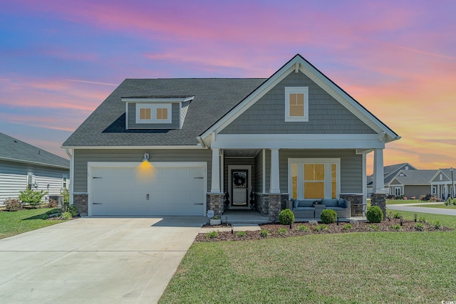 craftsman-style home with a yard, stone siding, covered porch, and a garage