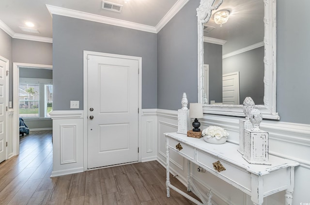 entrance foyer with a wainscoted wall, visible vents, wood finished floors, and ornamental molding