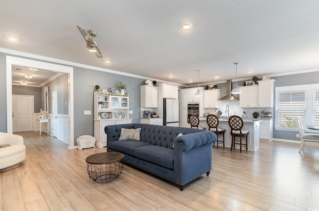 living area with a ceiling fan, recessed lighting, ornamental molding, wainscoting, and light wood-type flooring