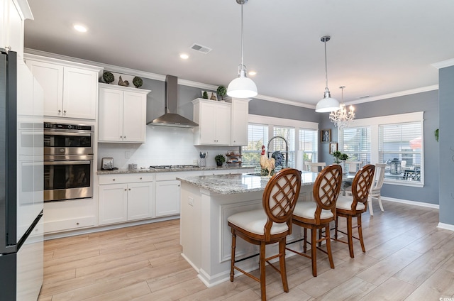 kitchen featuring a sink, wall chimney exhaust hood, light wood-style floors, white cabinetry, and appliances with stainless steel finishes