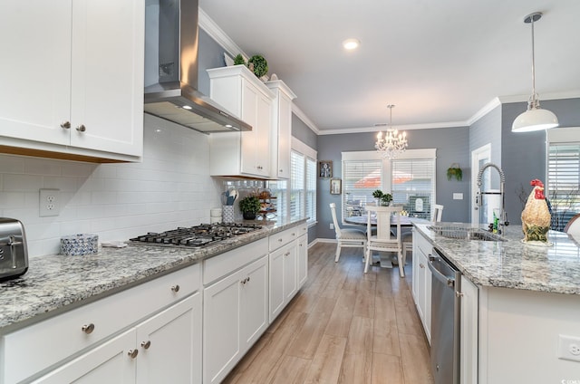 kitchen with an inviting chandelier, a sink, wall chimney exhaust hood, stainless steel appliances, and white cabinets