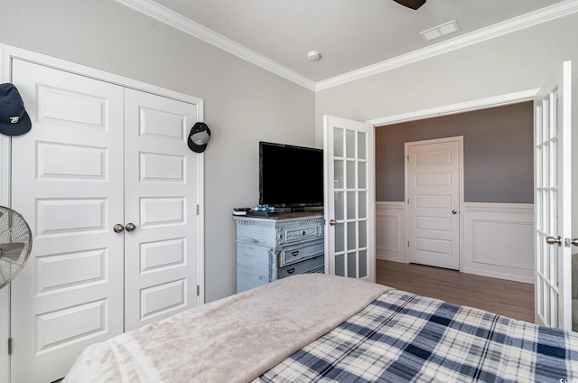 bedroom with wood finished floors, a wainscoted wall, a closet, visible vents, and ornamental molding