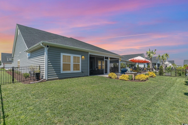 back of house at dusk featuring a yard, a sunroom, a shingled roof, and a fenced backyard